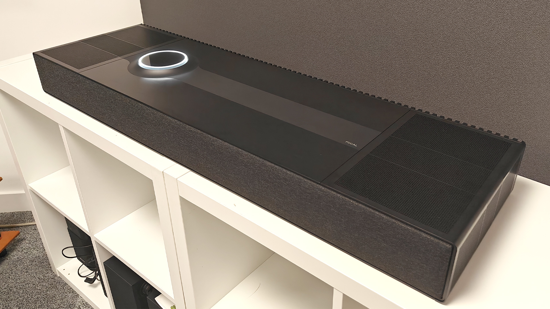 Focal Mu-so Hekla soundbar on white shelving unit in front of grey baffle