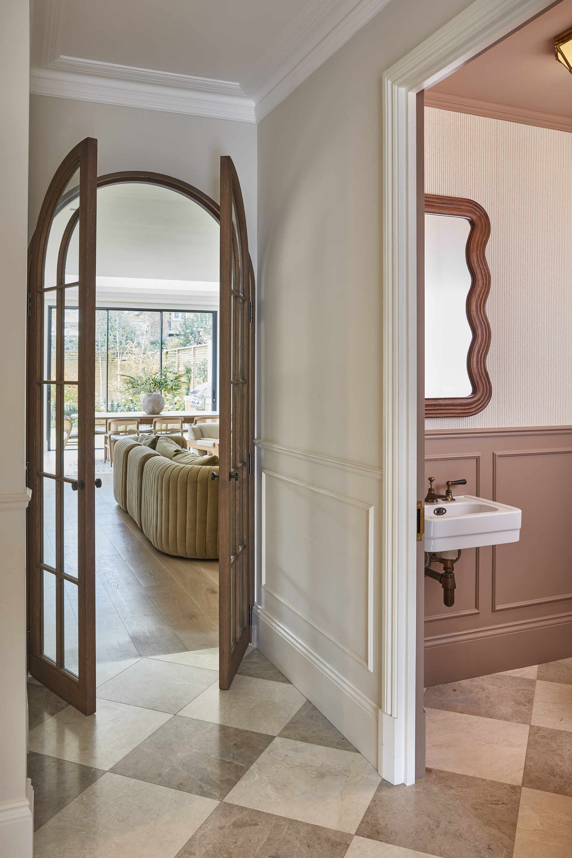 A bathroom with a pink and white marble checkerboard flooring and a view through the doorway into a living room