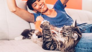 A smiling woman plays with her large cat on a white couch