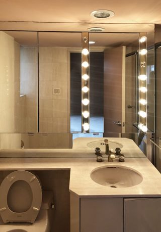 A dated bathroom with a large mirror fitted with bulbs