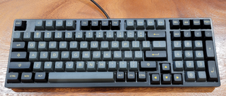 dark gray keyboard with light gray keycaps against medium wood background