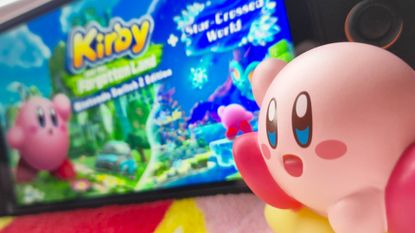 Photo by Rosalie Newcombe of a Kirby toy sitting in-front of a Switch 2 that's running Kirby and the Forgotten Land.