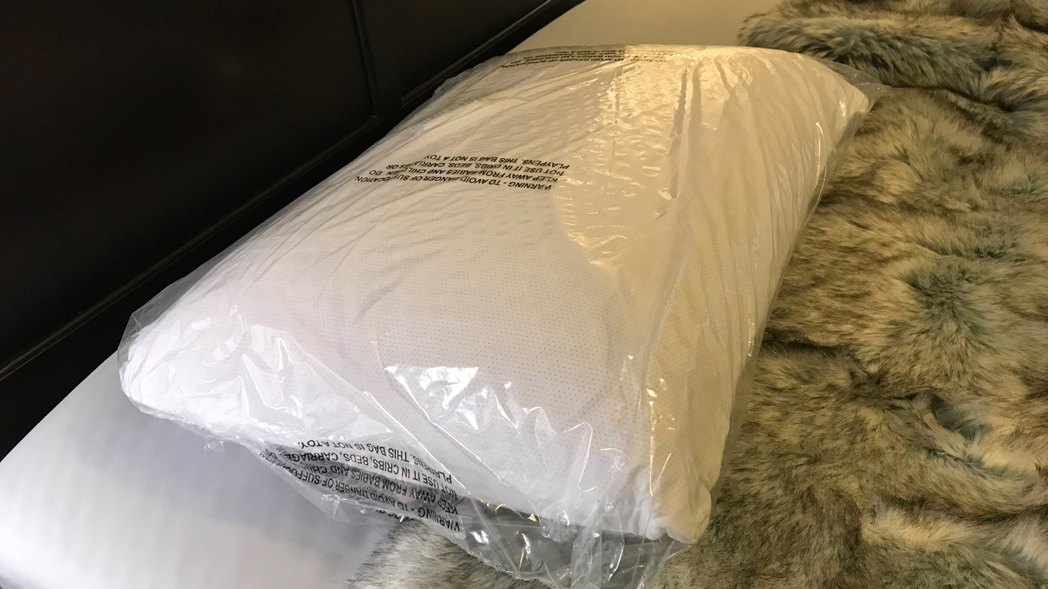 O Purple Harmony Pillow em uma cama em seu saco plástico