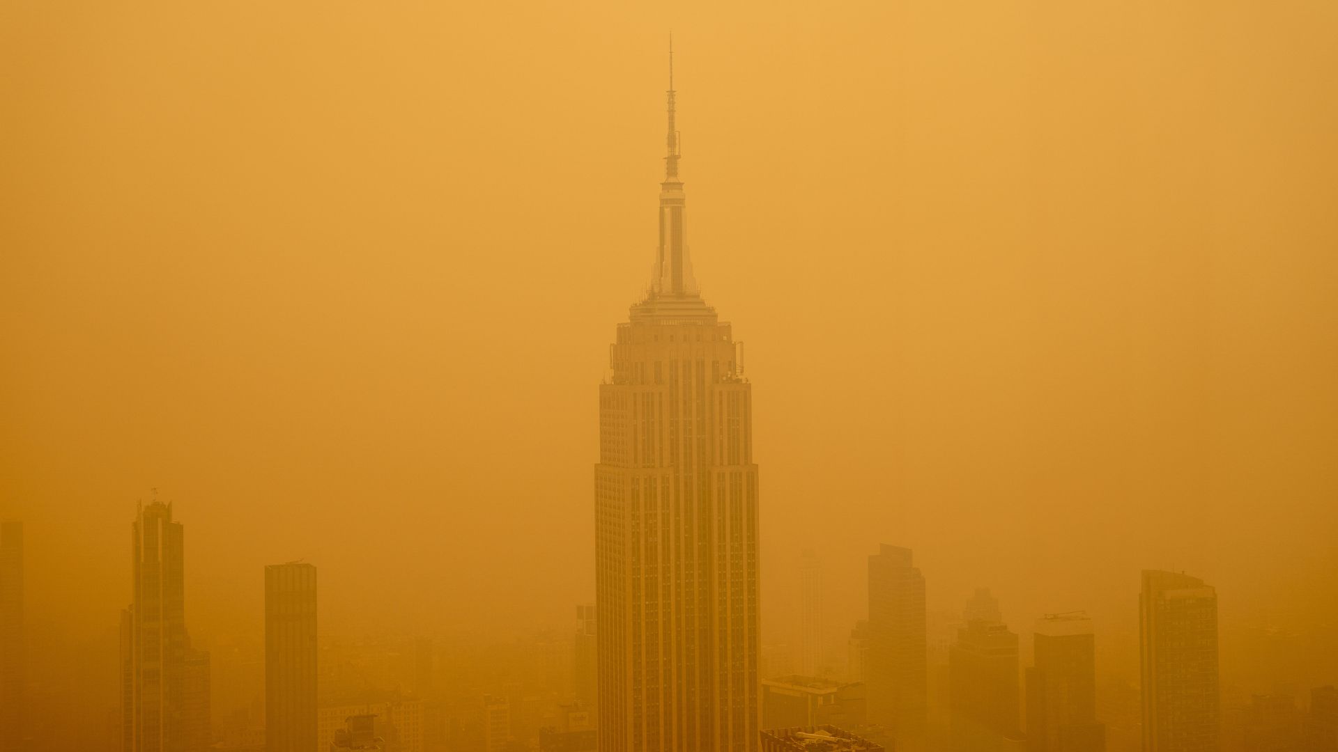 la foto muestra el Empire State Building visto desde un rascacielos cercano;  el edificio y los que están cerca están rodeados por una densa nube de smog de color amarillo anaranjado formada por el humo de los incendios forestales
