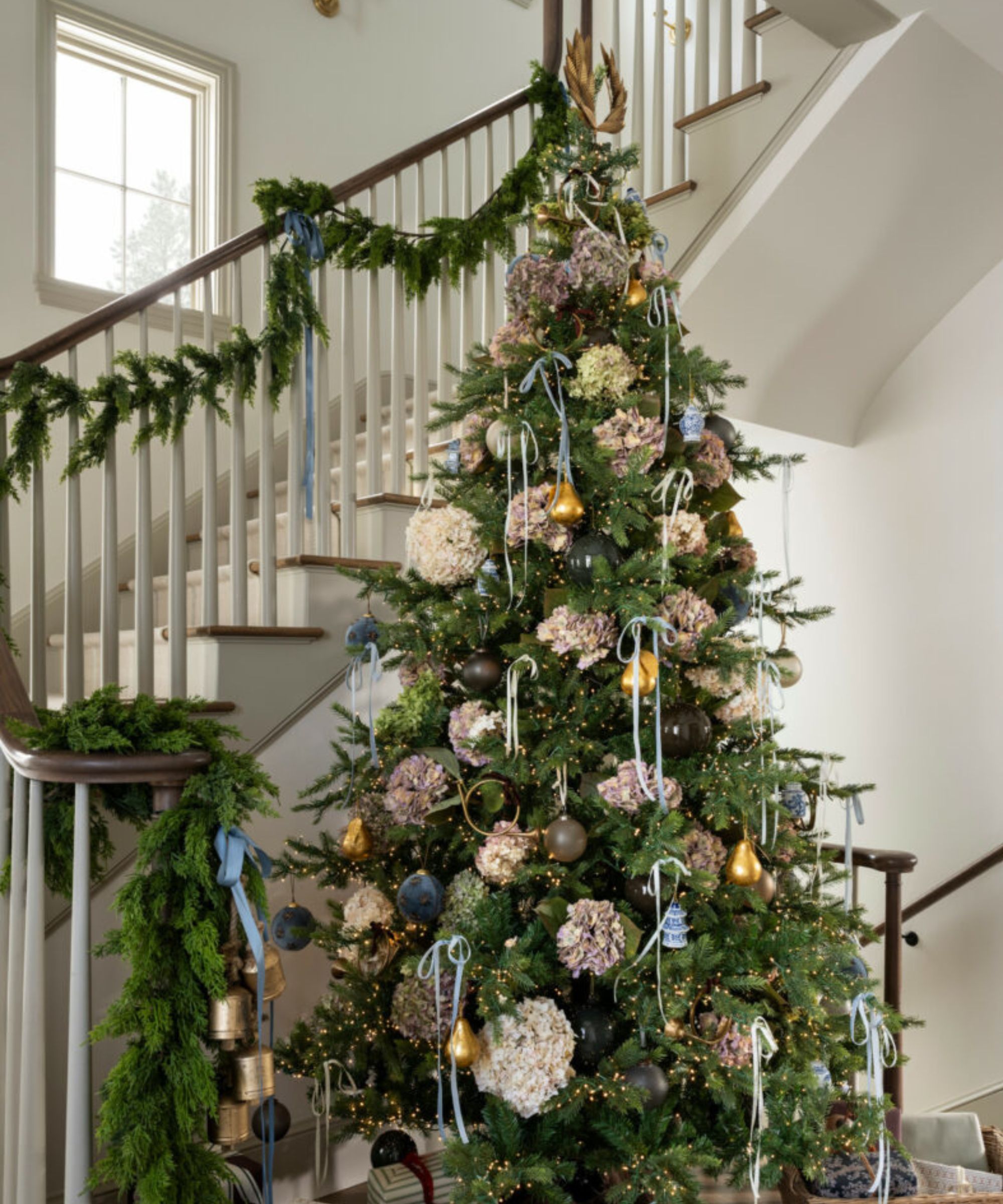 Christmas tree in entryway with hydrangeas and bows and garland on banister