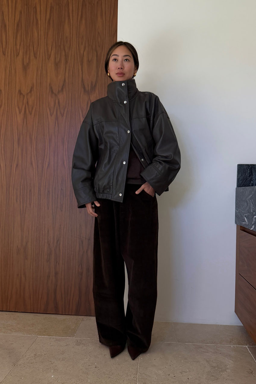 A woman wearing a black leather high collar jacket and black pants