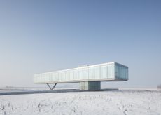 A flat and wide building of concrete, metal and glass dutch house stands alone in a field of snow.