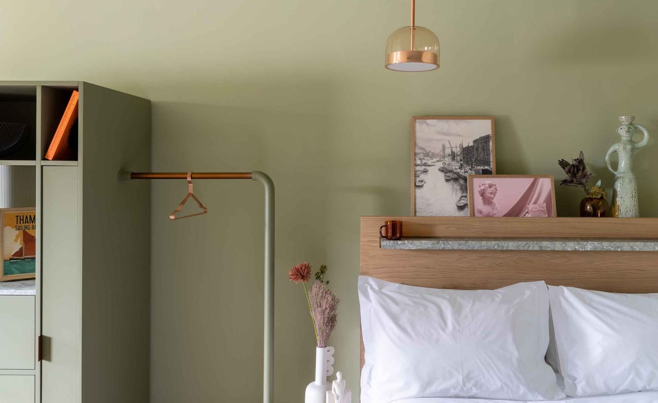 A room in the Locke at Broken Wharf Hotel. Olive green walls and closet, with various decorations on the wooden bedframe that has white linen.