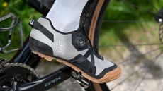Close up of a foot wearing white socks and grey shoes clipped into a pedal on a black gravel bike