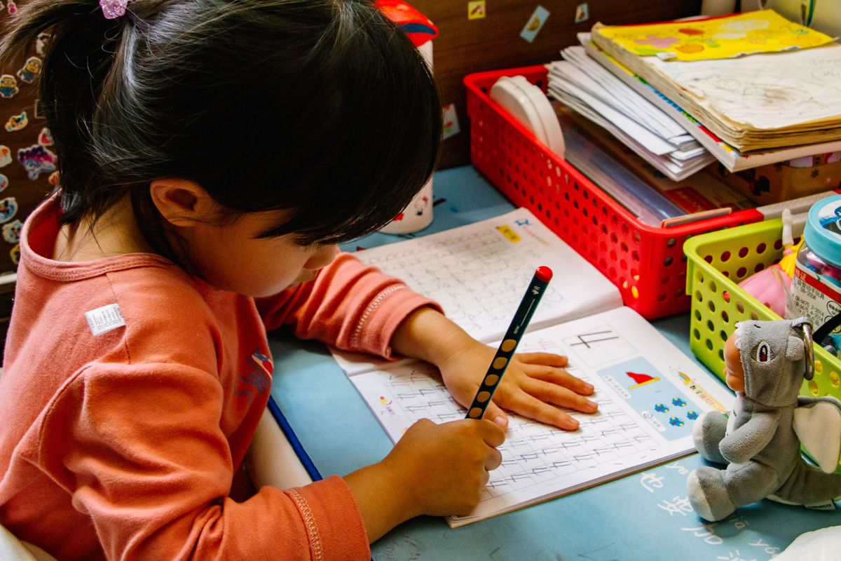 A young girl studies on a lightly blue desk at what appears to be a school.