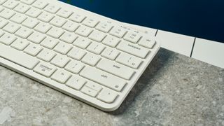 a close up shot of a white wireless bluetooth keyboard resting on a clean white table with a shadow underneath