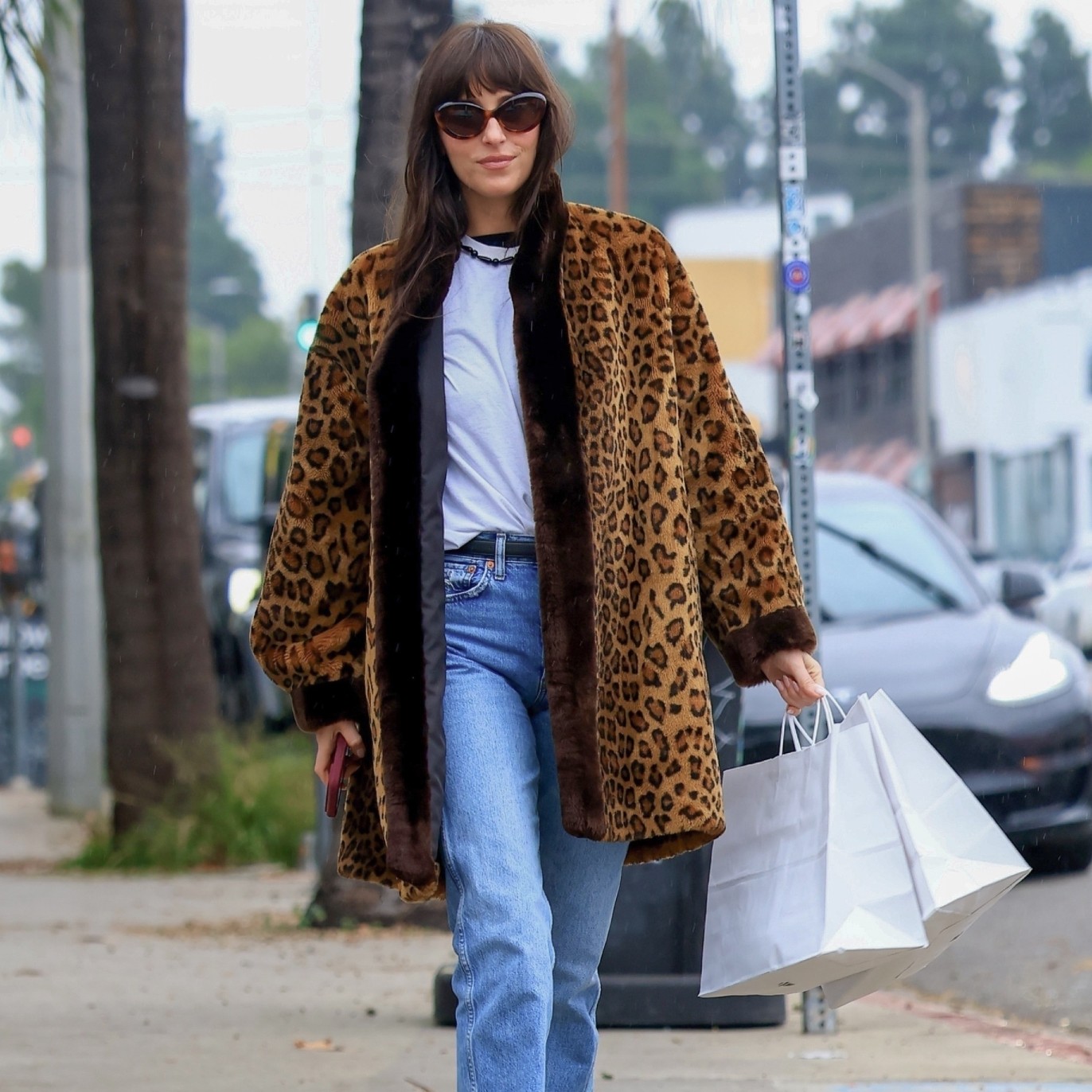 Dakota Johnson wears vintage Levi jeans, leopard coat, white t-shirt and oval sunglasses while shopping in LA.