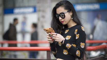 Lady wearing big sunglasses and a teddy bear sweater looking at her phone