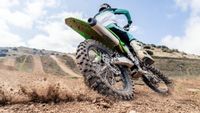Rear biker riding a motocross bike, kicking up mud and dust at the camera as they turn - stock photo