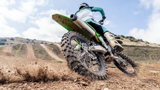 Rear biker riding a motocross bike, kicking up mud and dust at the camera as they turn - stock photo