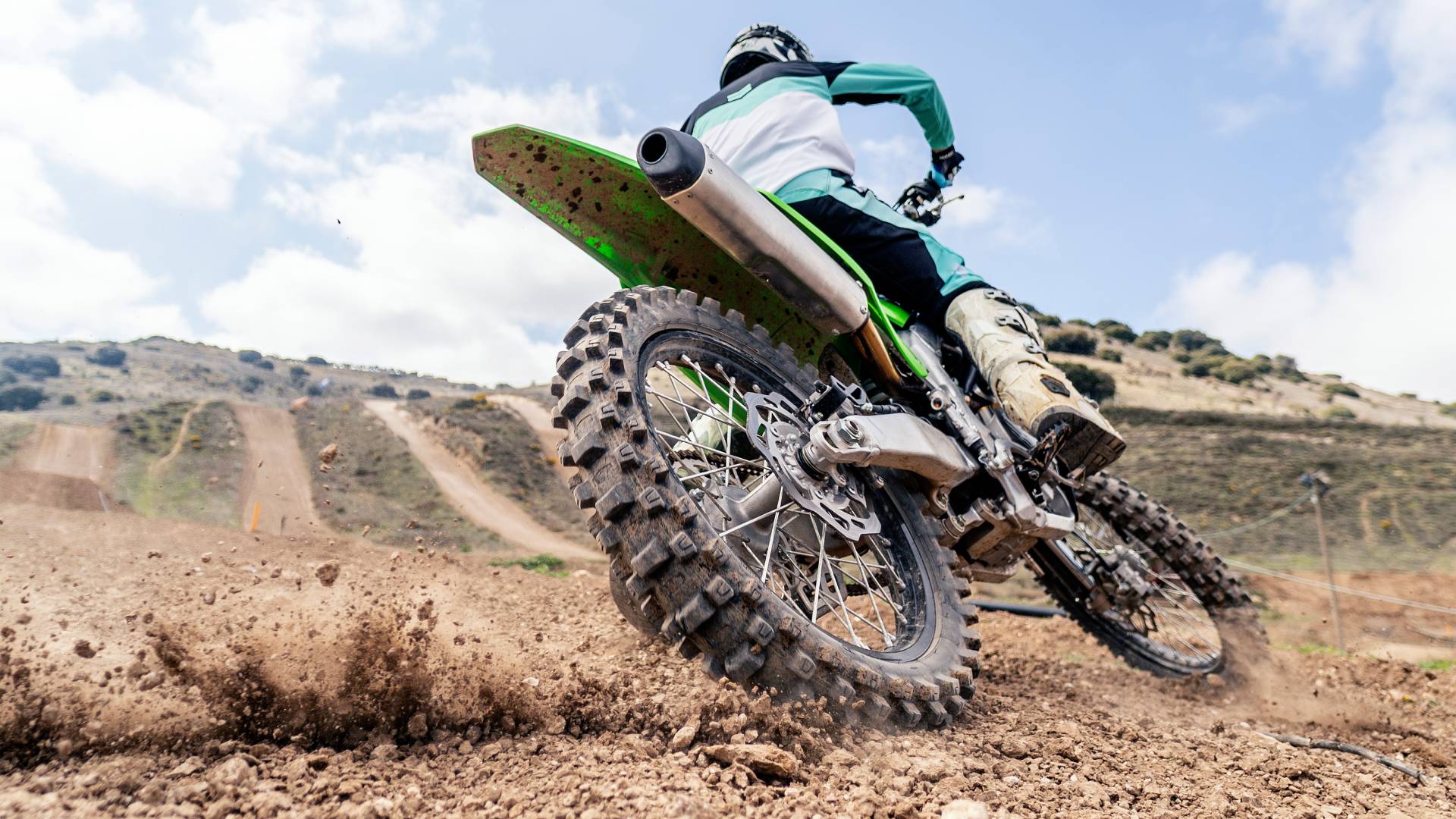 Rear biker riding a motocross bike, kicking up mud and dust at the camera as they turn - stock photo