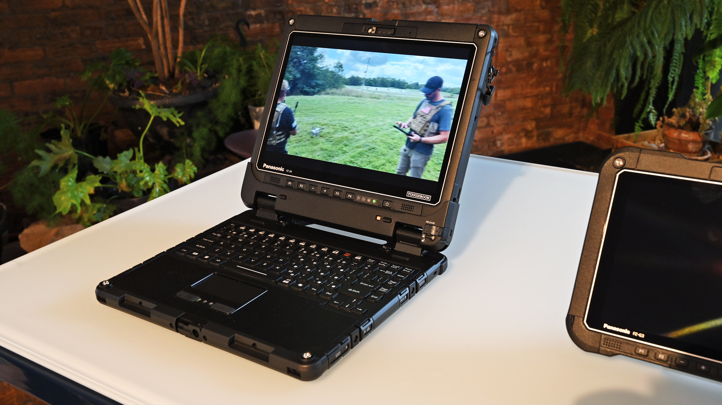 Open Panasonic TOUGHBOOK 34 laptop on a table playing video footage of drone operators outdoors.