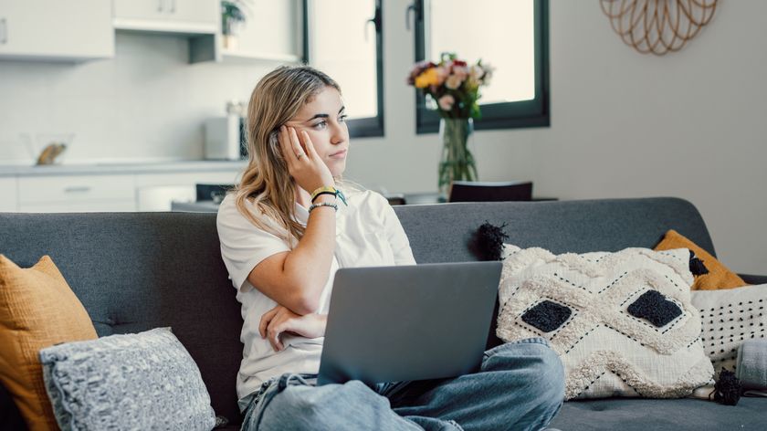 A woman sitting cross-legged on a couch in a well lit room with a laptop opened in her lap 