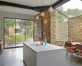 A kitchen with a white island and an exposed brick wall next and stylish glass windows and doors
