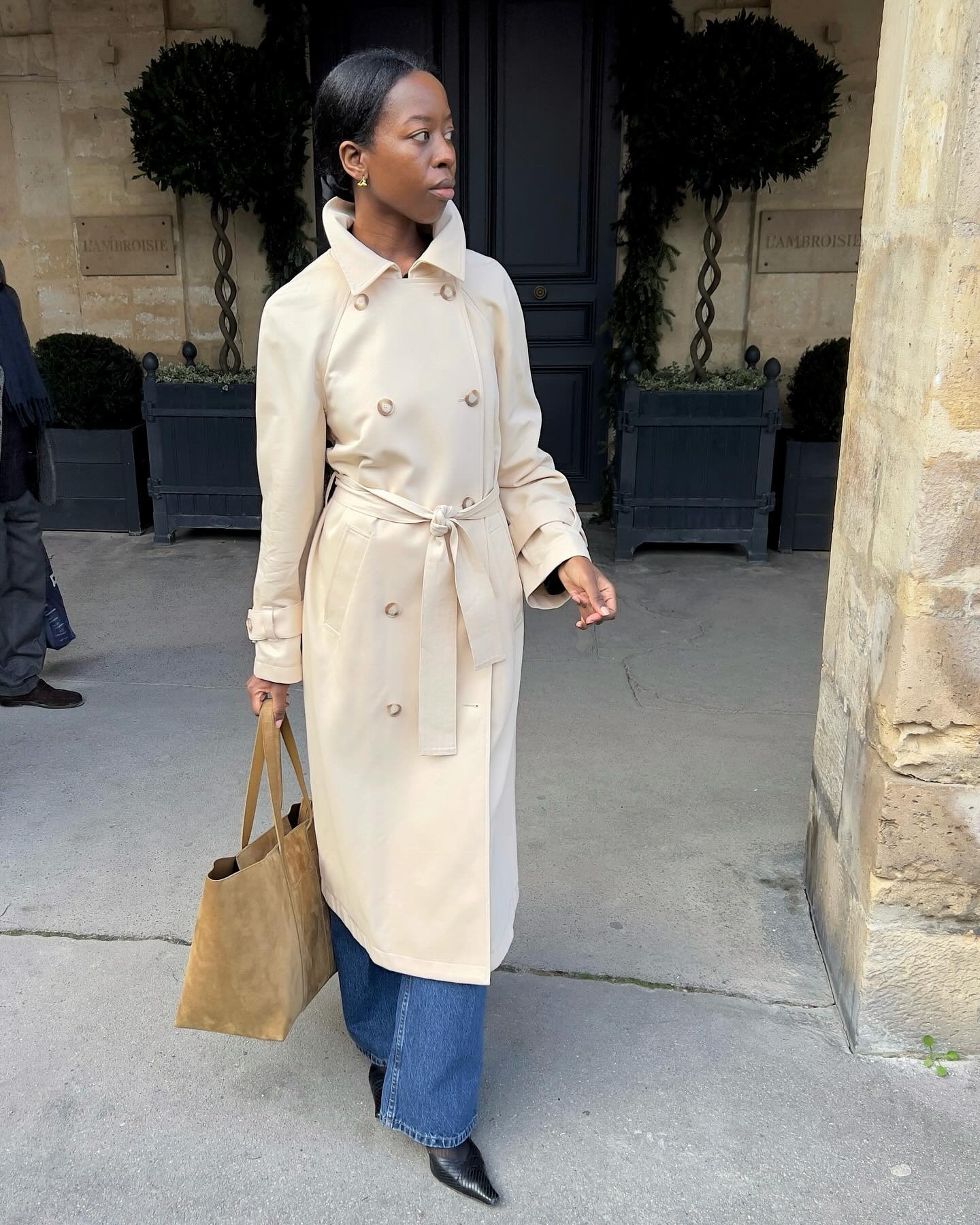Sylvie wears a trench coat, jeans, pumps and suede tote bag.