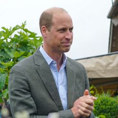 Prince William wears a gray suit and light blue tie and holds his hands together while looking pensive
