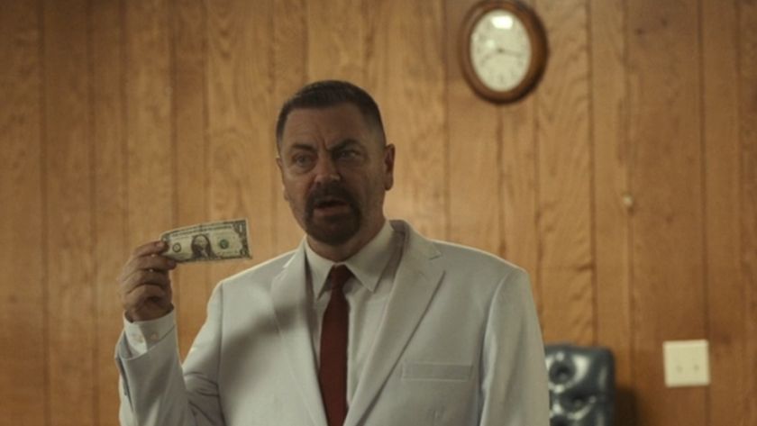 Nick Offerman in Sovereign, wearing a white suit and holding up a dollar bill. 