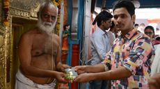 Indian Hindu devotee Rajashekar Reddy (R) receive his passport after it is blessed by a priest at the Chilkur Balaji Temple