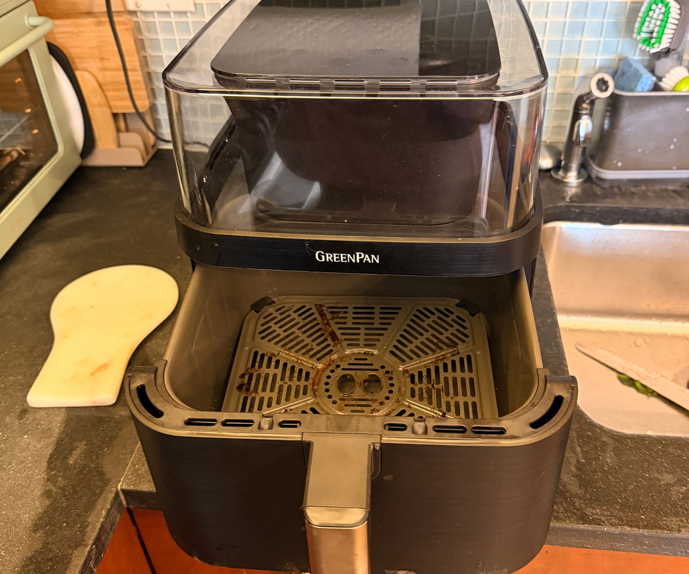 The GreenPan Bistro 360 Air Fryer open on the counters with a dirty draw, beside a kitchen sink
