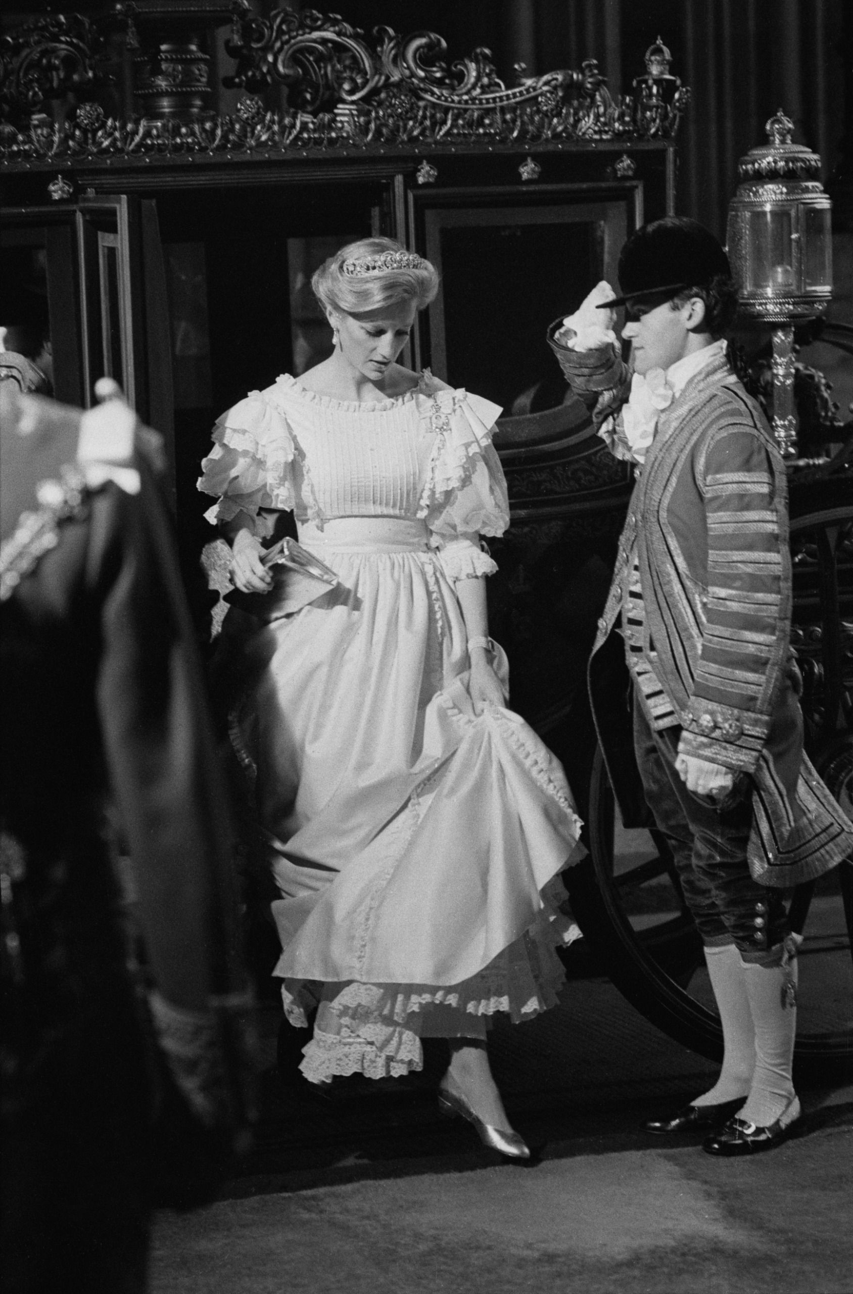 Princess Diana wearing a long white dress and a tiara being saluted by a footman