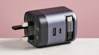 UGreen Nexode 65W Charger with Retractable USB-C Cable on its side against pink background