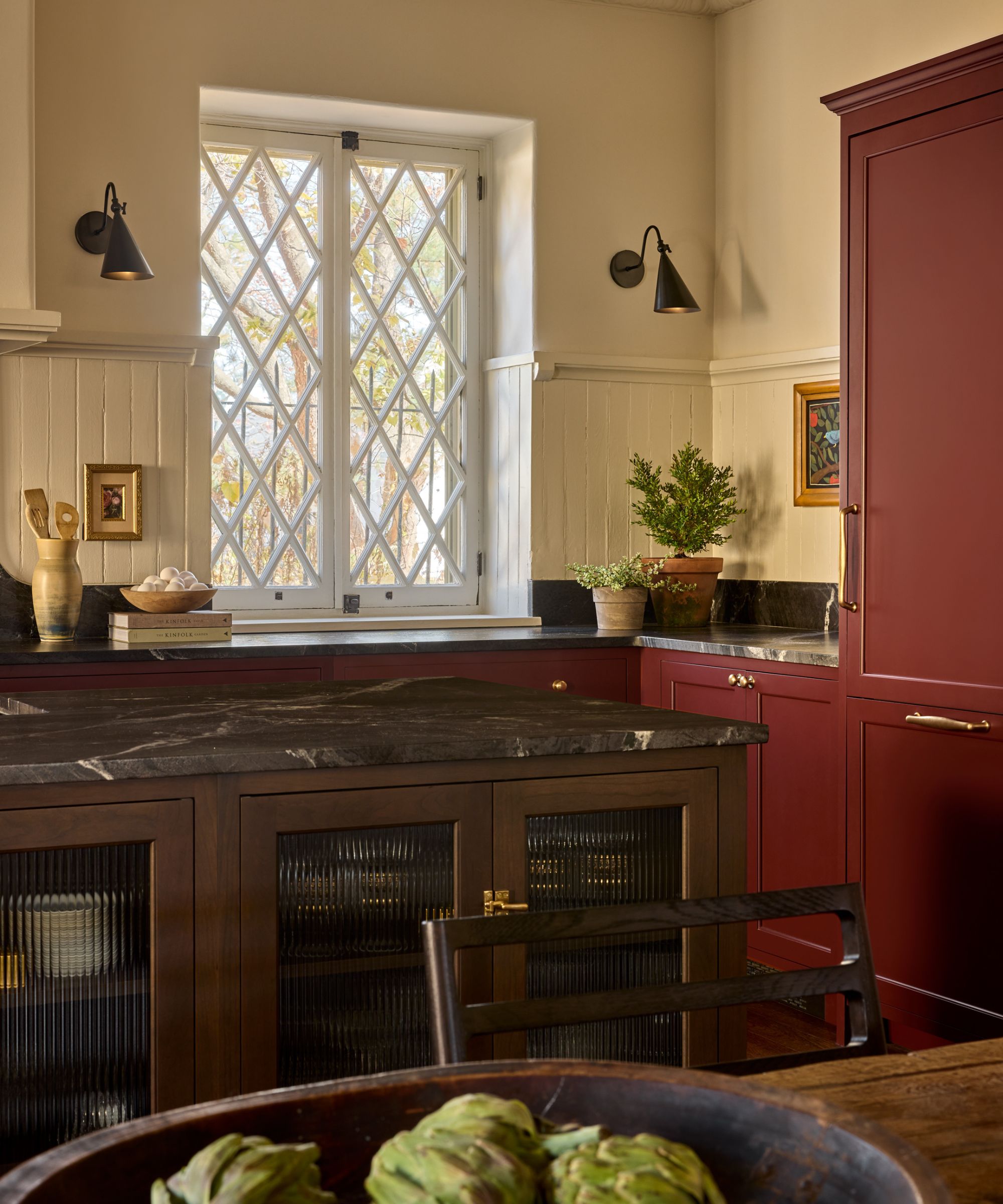 Cream kitchen with dark red cabinets, dark marble countertops and dark wooden island