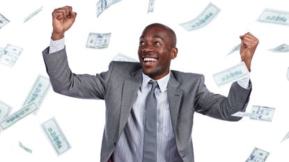 A man in a suit celebrates as cash rains down on him.