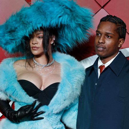 Rihanna in a huge furry teal hat and a black dress with furry teal wrap, and A$AP Rocky in a white shirt, red tie, and navy jacket at the 2024 Fashion Awards