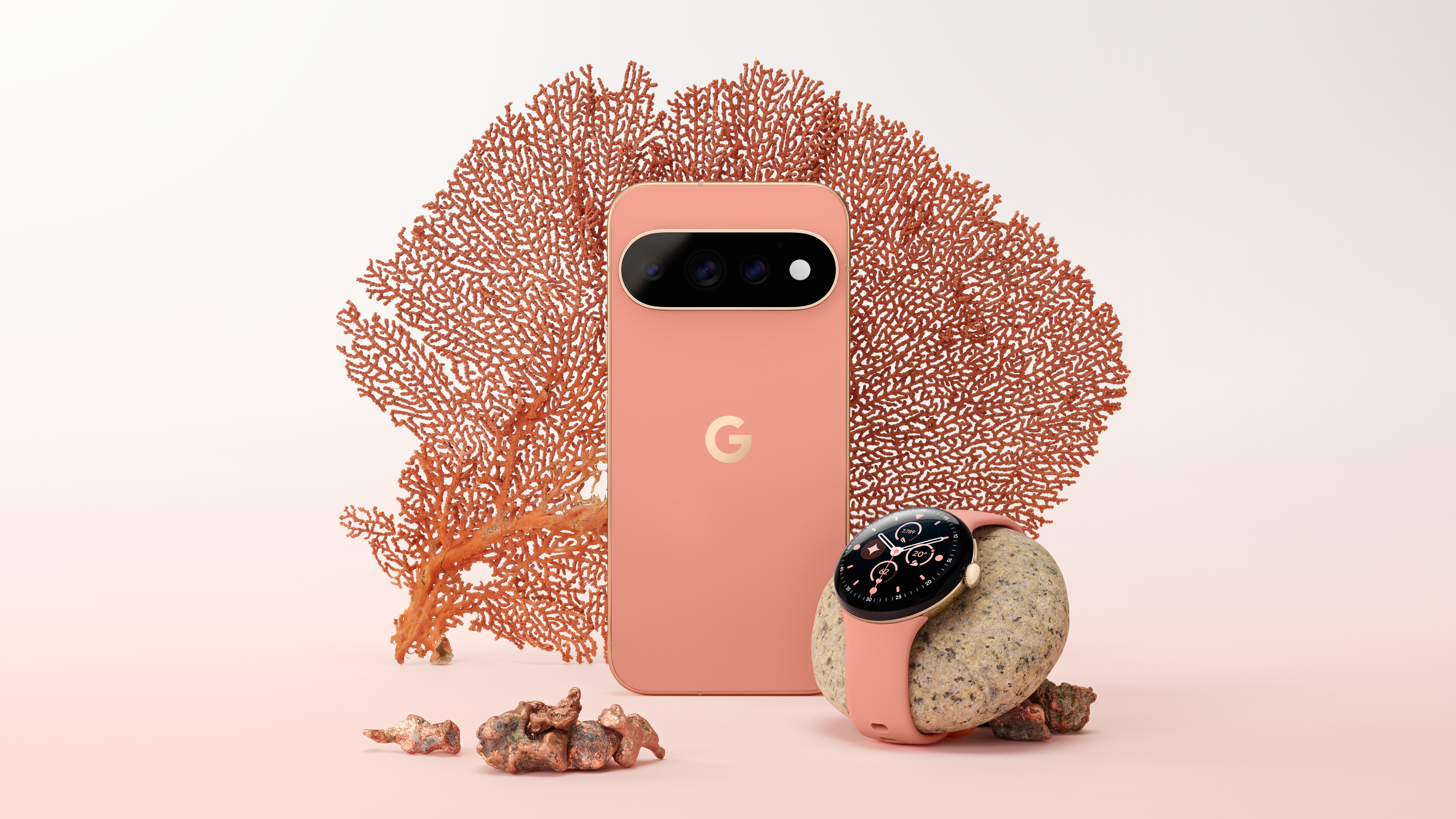 A pink and gold Google Pixel 11 Pro on a white/pink gradiant background with a piece of coral