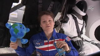 NASA astronaut Anne McClain welcomes SpaceX's first Crew Dragon to the International Space Station in a video message recorded inside the spacecraft on March 3, 2019. A test dummy "Ripley" sits behind her in a SpaceX spacesuit. SpaceX launched the dummy and the Earth Celestial Buddies plush toy on Crew Dragon Saturday.