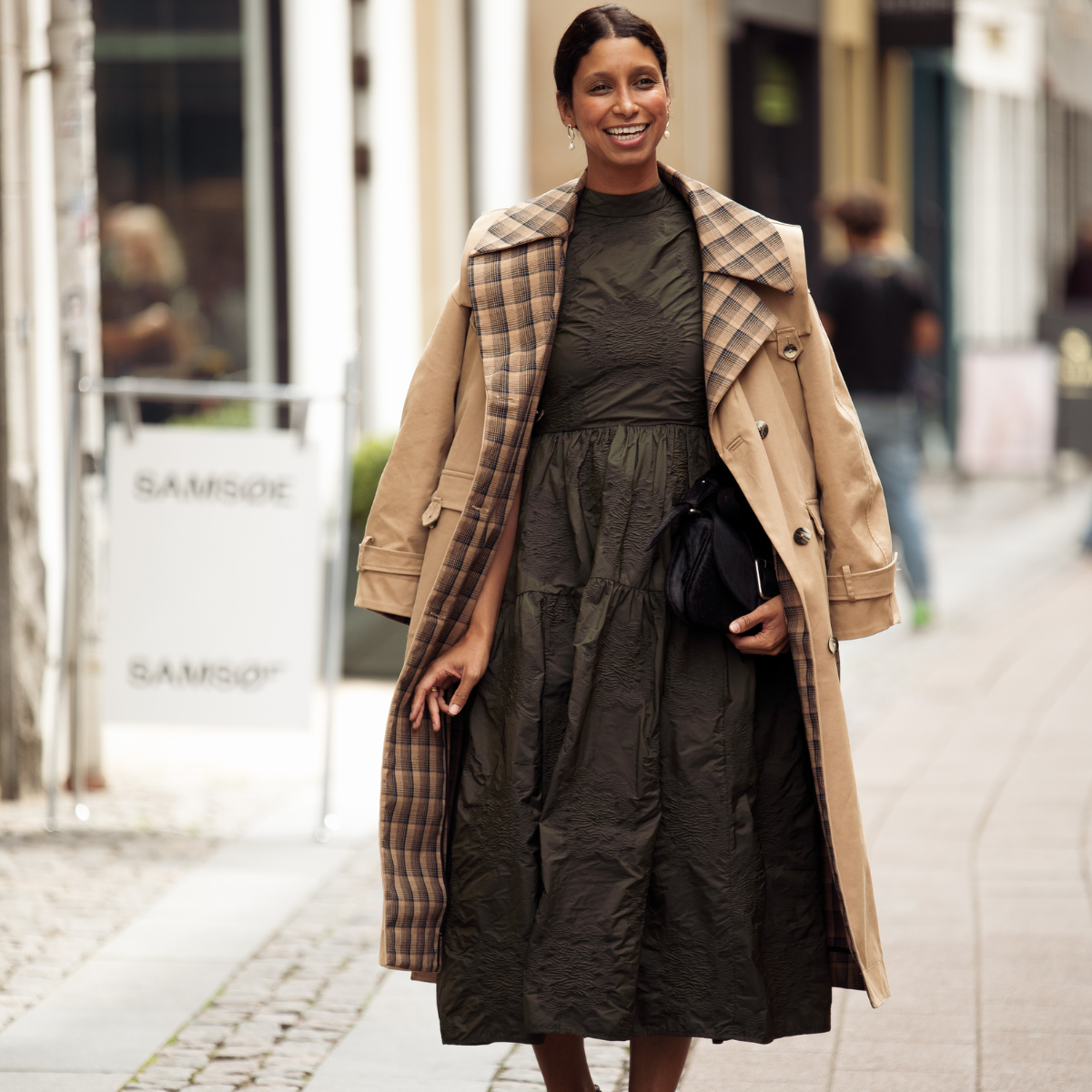 Miriam Akosua Nehring wears long khaki dress and brown trench coat outside Filippa K presentation during Copenhagen Fashion Week