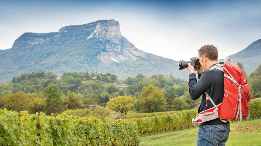 Photographer with a camera and backpack taking a picture of a mountain