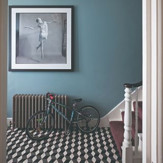 A blue-painted hallway with a black radiator, a child's bicycle and geometric tiles