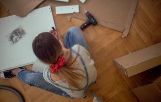 female sat on floor surrounded by pieces of cardboard and flat pack furniture