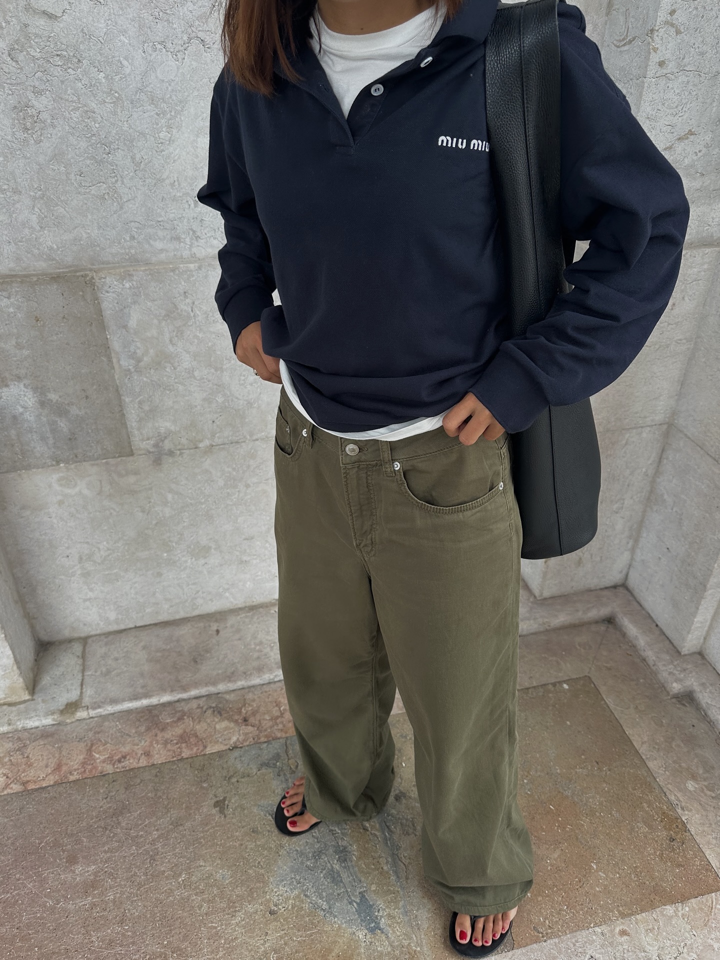 Woman wearing a white tee, a Miu Miu polo sweater, and green baggy jeans.