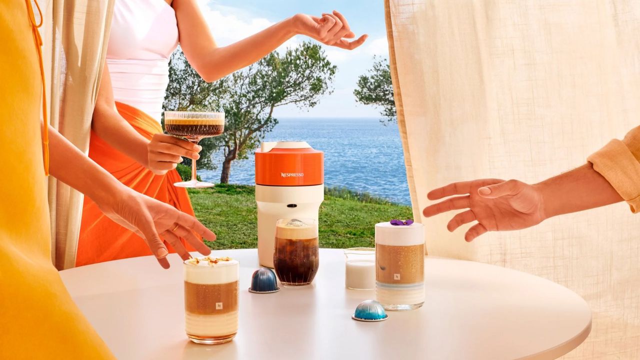 The Nespresso Vertuo Pop from the Pantone X Nespresso collection with iced coffees in front of it and coastline in the background