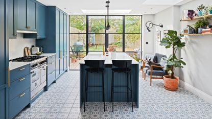 A bright kitchen with teal blue cupboards and a patterned tile floor