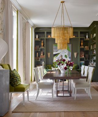 Green dining room with walnut style table and white chairs, besoke fretwork and bookcases at one end, large pendant light,