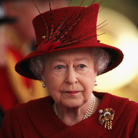 Queen Elizabeth wears a scarlet coat and matching hat with feathers in it and looks tearful