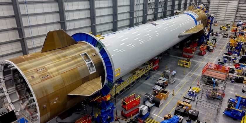 A long fuselage lays on the left on the floor of a large factory..