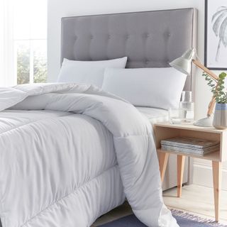 A white duvet and pillows on an upholstered bed with a wooden side table