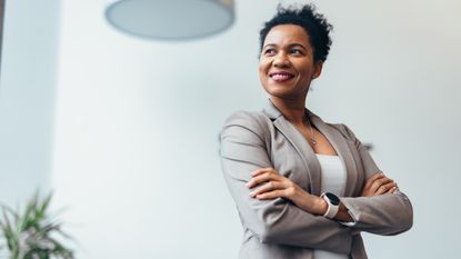 A business owner stands in her office with her arms crossed as she looks into the distance.