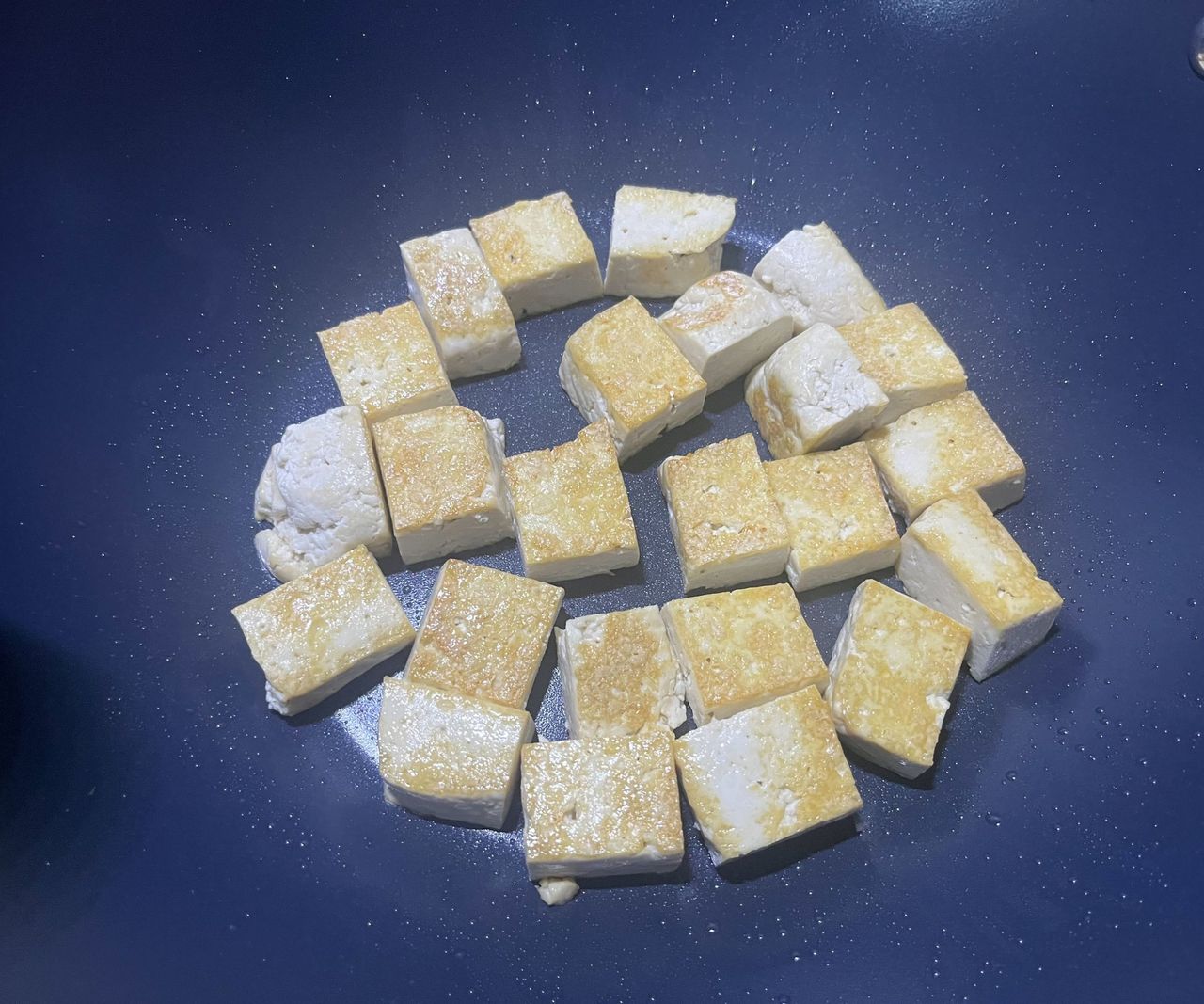 Cubes of golden fried tofu in the base of a blue ceramic pan