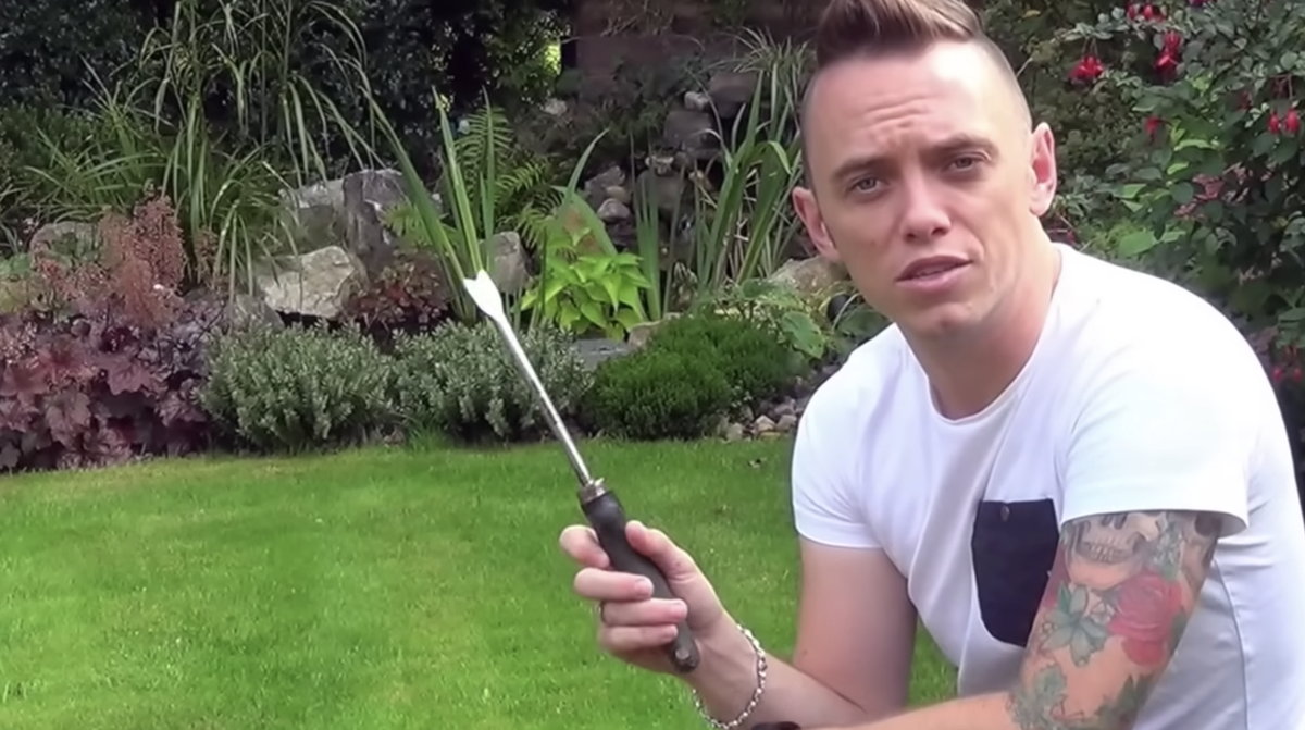 A man on a garden lawn holds up a dandelion weeder tool 