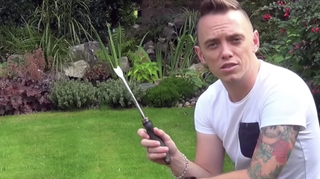 A man on a garden lawn holds up a dandelion weeder tool